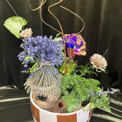 Mixed floral arrangement in a striped bowl with blue blooms and decorative accents