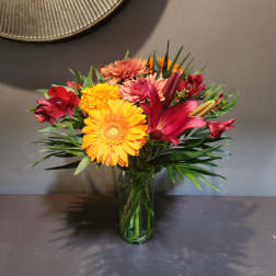Mixed bouquet of bright gerbera daisies, lilies, and alstroemeria in a glass vase