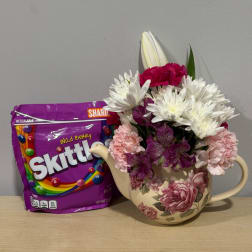 Mixed bouquet in a floral teapot vase beside a purple Skittles bag