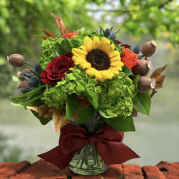 Bouquet with a sunflower, red and orange roses, and green hydrangeas in a glass vase