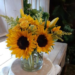 Sunflowers and yellow roses arranged in a clear glass vase