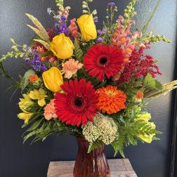 Colorful mixed bouquet in a brown glass vase with red gerberas and yellow roses