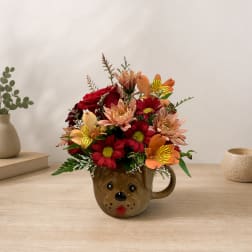 Mixed flower arrangement in a dog-face mug on a tabletop