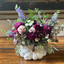 Mixed purple and pink flowers arranged in a white pumpkin-shaped vase