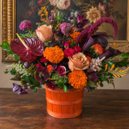 Mixed floral arrangement in an orange wooden basket with burgundy and peach blooms