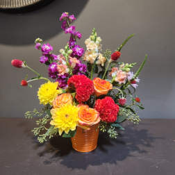Mixed bouquet in an orange vase with yellow, orange, red, and purple blooms
