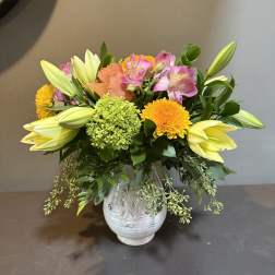 Mixed bouquet in a white ceramic vase with lilies, roses, and orange blooms