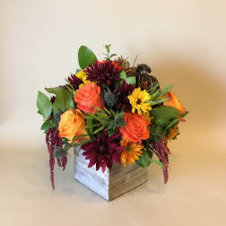 Mixed bouquet of orange and burgundy flowers in a wooden box