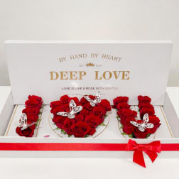 Red roses arranged in a white gift box with butterfly decorations and a red ribbon