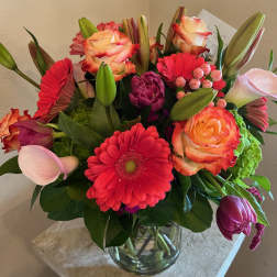 Mixed bouquet of pink, coral, and red flowers in a glass vase
