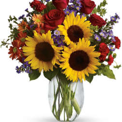 Bouquet of sunflowers, red roses, and purple daisies in a clear glass vase
