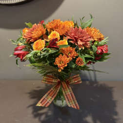 Bouquet of orange and red flowers in a glass vase with a plaid ribbon