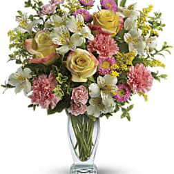 Mixed bouquet of roses, carnations, alstroemeria, and yellow filler flowers in a glass vase