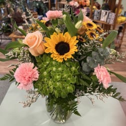 Mixed bouquet with sunflowers, peach roses, pink carnations, and a glass vase