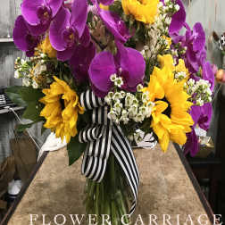 Bouquet of purple orchids and yellow sunflowers in a glass vase with a striped ribbon