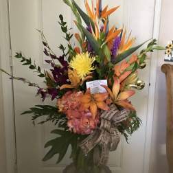 Tropical bouquet with orange bird-of-paradise and mixed blooms in a glass vase