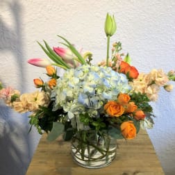 Mixed bouquet with blue hydrangea, orange roses, and pink tulips in a glass vase