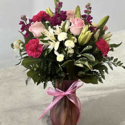 Pink and white mixed flower bouquet in a pink vase with a ribbon