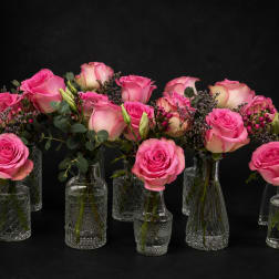 Pink roses arranged in small clear glass vases with greenery