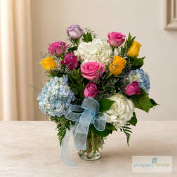 Mixed bouquet of roses and hydrangeas in a glass vase with a blue ribbon