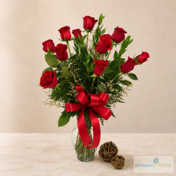 Red roses arranged in a clear glass vase with a red ribbon