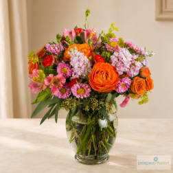 Mixed bouquet of orange, pink, and white flowers in a clear glass vase