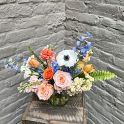 Mixed bouquet of roses, tulips, and blue flowers in a glass vase