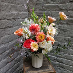 Mixed bouquet of coral, peach, and white flowers in a white vase