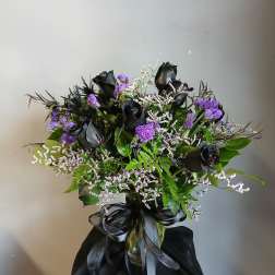 Black roses and purple filler flowers in a glass vase with a black ribbon