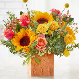 Bright bouquet of sunflowers, roses, and succulents in a textured square vase