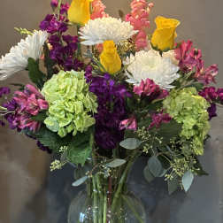 Mixed bouquet of yellow roses, white mums, and pink and green blooms in a clear glass vase
