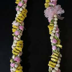Floral lei with pink buds, yellow flowers, and white beads on a black background