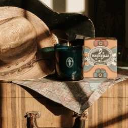 A straw hat beside a lit candle and a Nashville gift box on a suitcase