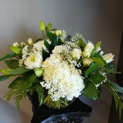 White floral arrangement in a glass vase with lilies, roses, and hydrangeas
