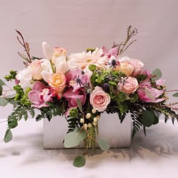 Low pastel arrangement of roses, orchids, and mixed blooms in a white wooden box.
