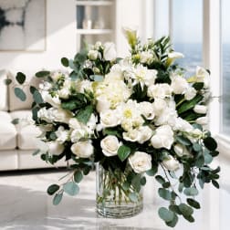 White floral arrangement in a clear glass vase with trailing eucalyptus