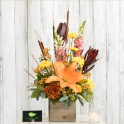 Orange lily arrangement in a wooden box with yellow and burgundy accents