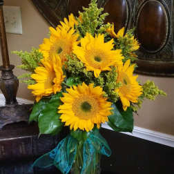 Bouquet of bright yellow sunflowers with a teal ribbon in a glass vase