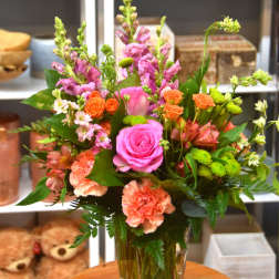 Tall mixed bouquet with pink roses, peach carnations, and orange spray roses in a clear glass vase