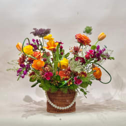 Colorful mixed flower arrangement in a wicker basket with a pearl garland