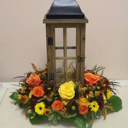Lantern centerpiece surrounded by orange, yellow, and burgundy flowers