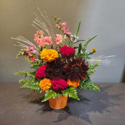 Mixed floral arrangement in a ribbed orange pot with pink, yellow, and dark blooms