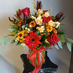 Mixed bouquet of red, yellow, and cream flowers in a glass vase with a red ribbon