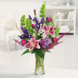 Tall mixed bouquet with pink lilies, purple irises, and green spikes in a glass vase