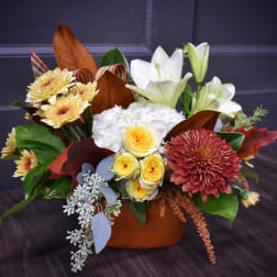 Mixed bouquet with white lilies, yellow roses, and chrysanthemums in a brown container