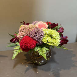 Mixed bouquet in a round glass vase with pink, red, and green blooms