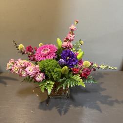 Colorful mixed bouquet in a square glass vase with pink, purple, and yellow blooms.