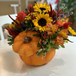 Fall floral arrangement in a pumpkin container with sunflowers and orange blooms