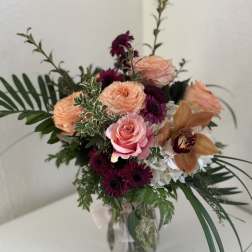 Mixed bouquet of roses, orchids, and purple blooms in a glass vase