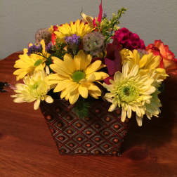 Yellow daisies and mixed flowers arranged in a patterned square container